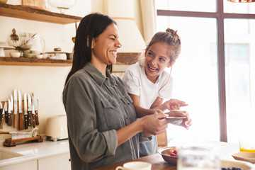 Wall Mural - image of beautiful family woman and her little daughter cooking together meal with raspberry at cozy