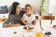 © Drobot Dean - Image of joyous family mother and little daughter smiling and eating together while having breakfast at home in morning