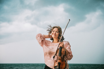 Outdoor portrait of beautiful woman with violin, dark rainy day