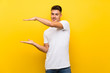 © luismolinero - Young handsome man over isolated yellow background holding copyspace to insert an ad
