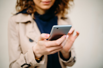 Wall Mural - Woman with curly hair in a beige coat with a phone