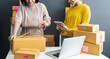 © sutthinon602 - Women packing parcels with sticky tape, Entrepreneur owner using smartphone or laptop taking receive and checking online purchase shopping order to preparing pack product box. Selling online ideas con