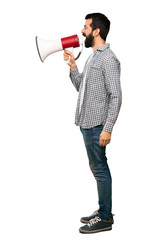 Wall Mural - Handsome man with beard shouting through a megaphone over isolated white background