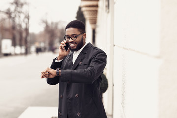 Handsome businessman looking at watch and talking on cellphone