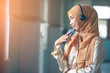 © rachaphak - Portrait of a smiling young modern arabian woman holding mobile phone and listening the music to headphone.