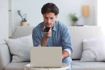 Poster - Serious Man Using Phone Voice Assistant Sitting At Laptop Indoor