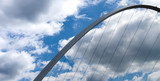 Abstract image of the Gateshead Millennium Bridge showing the arch of the bridge against a cloudy blue sky with cables heading towards the bottom of the image.