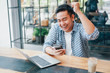 © chayathon2000 - Asian young man in blue shirt working with laptop computer and mobile phone with online job or shopping online happy and smile face in coffee shop cafe