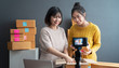 © sutthinon602 - Beautiful asian woman blogger showing clothes in front of camera to recording vlog video live streaming at her shop. Business online influencer on social media concept. Online Selling. Online Shopping