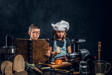 Wall Mural - Little girl and boy are cooking vegetables and reading old recipe book.