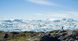 Travel wanderlust adventure in Arctic landscape nature with icebergs - tourist person looking at view of Greenland icefjord - aerial photo. Man by ice and iceberg, Ilulissat Icefjord.