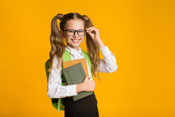 Wall Mural - Schoolgirl Standing Holding Schoolbooks Over Yellow Background