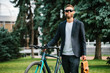 © San4ezz007 - A young stylish hipster businessman going to work by bike on urban street.