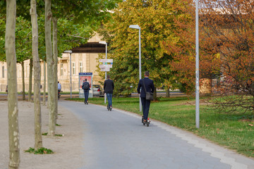 Wall Mural - Group of officer ride E-scooters from startup company with idea of Eco friendly mobility for urban lifestyle by sharing Electric Scooter, on bicycle lanes in the park in Düsseldorf, Germany.