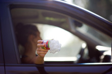 Girl Holds Trash Outside The Car Window. A Woman Is About To Throw Waste Out Of A Car. Environmental Pollution, Selective Focus, Backlight