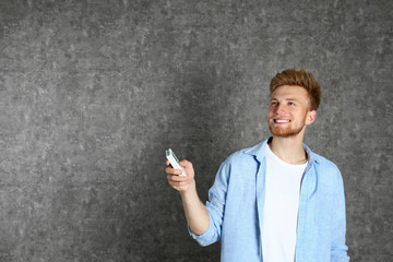 Wall Mural - Young man with air conditioner remote on grey background. Space for text