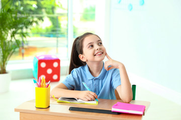 Poster - Pensive little girl doing assignment at desk in classroom. School stationery