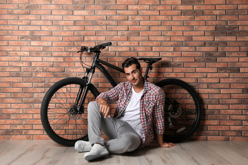 Wall Mural - Handsome young man with modern bicycle near brick wall indoors