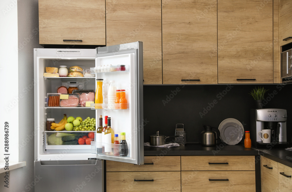 Open refrigerator full of products in kitchen - obrazy, fototapety, plakaty 