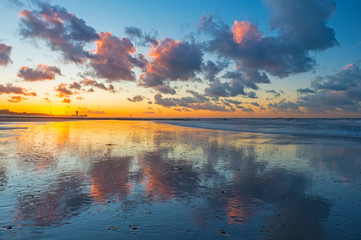 Sunset along the beach of Ostend (Oostende in Dutch) with a dramatic cloud reflection by the North Sea and the urban cityscape in the background, West Flanders, Belgium.