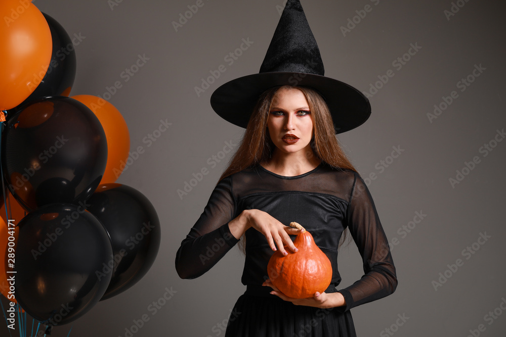 Beautiful woman dressed as witch for Halloween on grey background