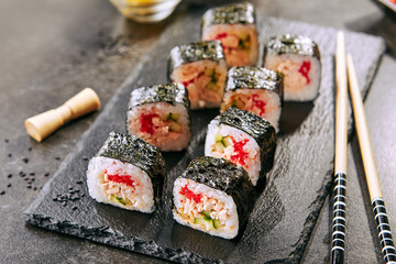 Canvas Print - Macro shot of sushi roll in Japanese restaurant with chopsticks closeup. Sushi rolls with rice, fried salmon, flying fish caviar, cucumber and spicy sauce