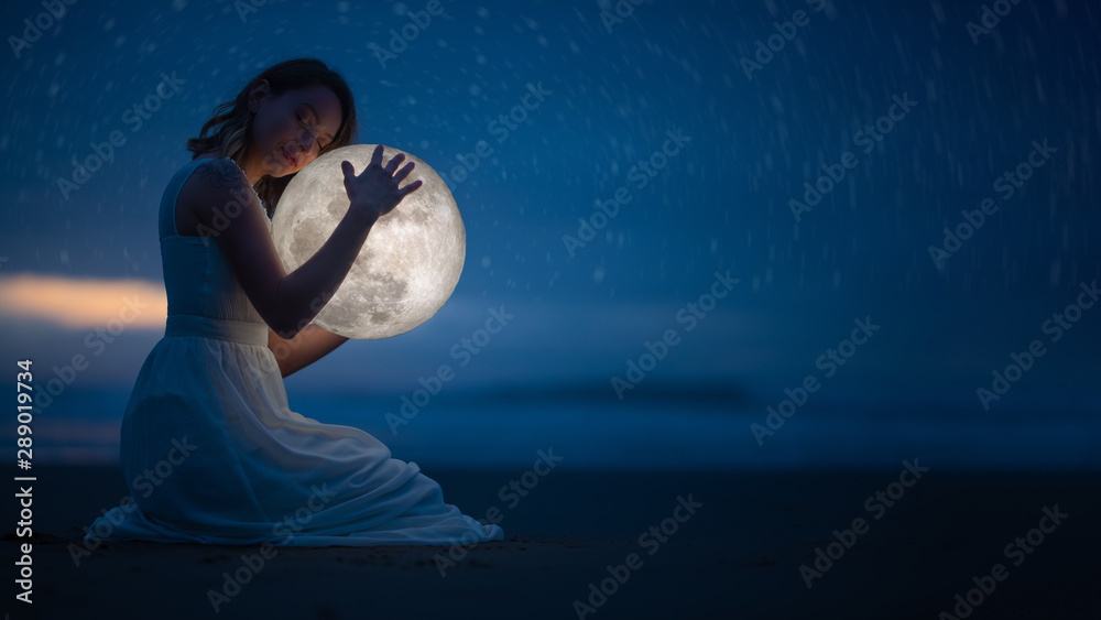 Tender image of a girl; female magic. Beautiful attractive girl on a night beach with sand and stars hugs the moon, art photo. On a dark background with space. - obrazy, fototapety, plakaty 