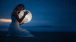 © Anton - Tender image of a girl; female magic. Beautiful attractive girl on a night beach with sand and stars hugs the moon, art photo. On a dark background with space.