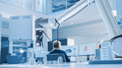 Aufkleber - Modern Robot Arm Picks up, Lifts and Moves Metal Component as Programmed. In the Background Industrial Robotics Engineers Working on Software, Programming and Machine Learning in Engineering Facility