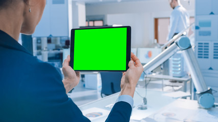 Aufkleber - Engineer Holds Green Mock-up Screen Digital Tablet Computer. In the Background Team of Industrial Engineers Working with Functional Robot Arm in Modern Bright Research Facility