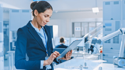 Wall Mural - Stylish Female Industrial Robotics Engineer Uses Tablet Computer to Program and Manipulate Robot Arm for Lifting, Moving Objects. Technology Research Facility for Machine Learning and Cloud Computing