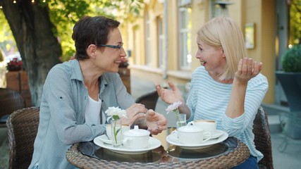 Wall Mural - Slow motion of mature ladies in casual clothing socializing in outdoor cafe talking laughing enjoying warm summer day. Friendship and happiness concept.