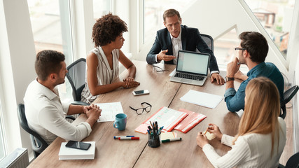 Teamwork. Serious mature man in formal wear showing something on the digital tablet and discussing something with his colleagues while sitting at the office table