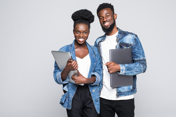 Portrait of a cheerful young african couple holding laptop computer while standing together and looking at each other isolated over gray background