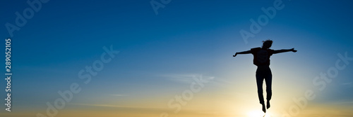 Fotografía Silhouette of a woman jumping in the sunset, panoramic sky background with copy