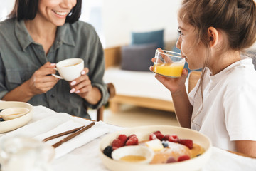 Wall Mural - image of smiling family mother and little daughter having breakfast at home in morning