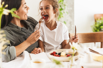 Wall Mural - image of caucasian family mother and little daughter eating tasty food together while having breakfa
