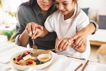 Wall Mural - image of lovely family mother and little daughter eating tasty food together while having breakfast 