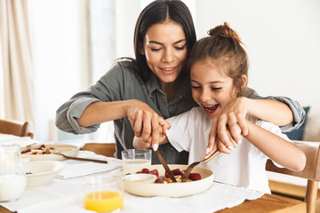 Image of amazing family mother and little daughter eating together while having breakfast at home in morning