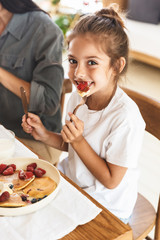 Wall Mural - image of pretty family mother and little daughter eating pancakes together while having breakfast at