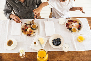 Wall Mural - cropped image from top of woman and little girl eating together while having breakfast at home in mo
