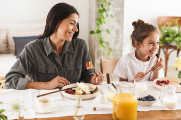 Wall Mural - image of joyous family mother and little daughter eating tasty food together while having breakfast 