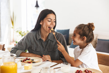 Wall Mural - image of gorgeous family mother and little daughter eating tasty pancakes together while having brea