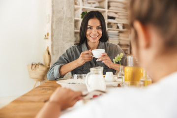 Wall Mural - portrait of positive family mother and little daughter in bright kitchen having breakfast at home in