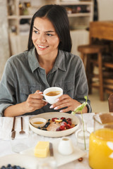 Wall Mural - portrait of beautiful brunette woman in bright kitchen having breakfast at home in morning