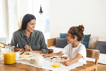 Wall Mural - image of positive family mother and little daughter having breakfast at home in morning