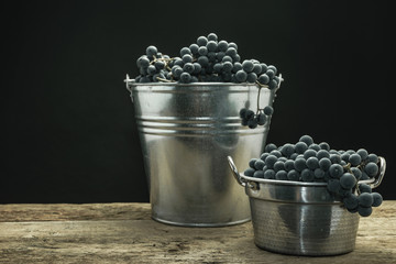 Poster - Beautiful wine grapes of silver basket on a old oak wooden table and black background.