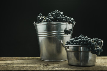 Poster - Beautiful wine grapes of silver basket on a old oak wooden table and black background.