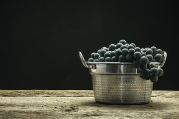 Poster - Beautiful wine grapes of silver basket on a old oak wooden table and black background.