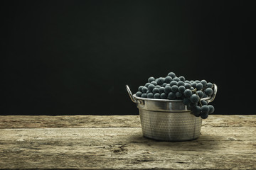 Poster - Beautiful wine grapes of silver basket on a old oak wooden table and black background.